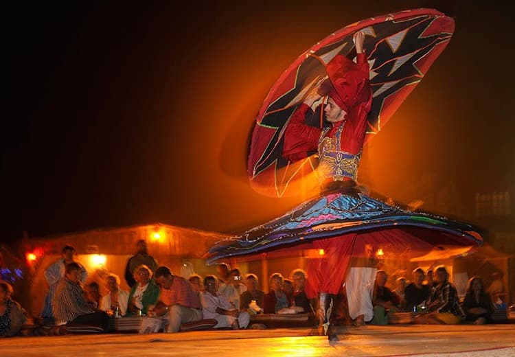 A dancer in vibrant red and blue traditional attire spins energetically, creating a swirling effect.
