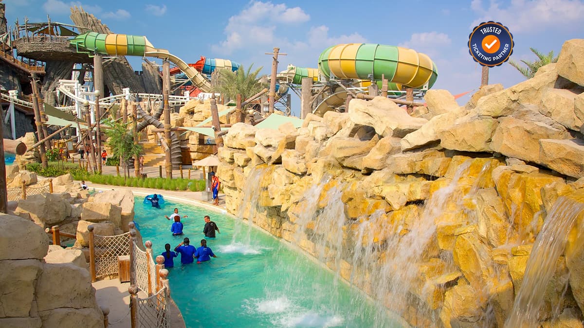 Group of six on a yellow raft ride in Yas Island water park, surrounded by colorful slides