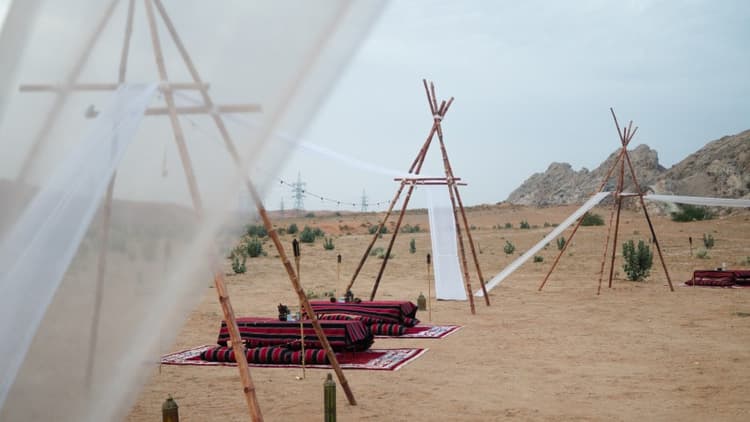 A tent with a canopy and a bed set up in the desert, with a buggy nearby for camp dinner during the daytime.