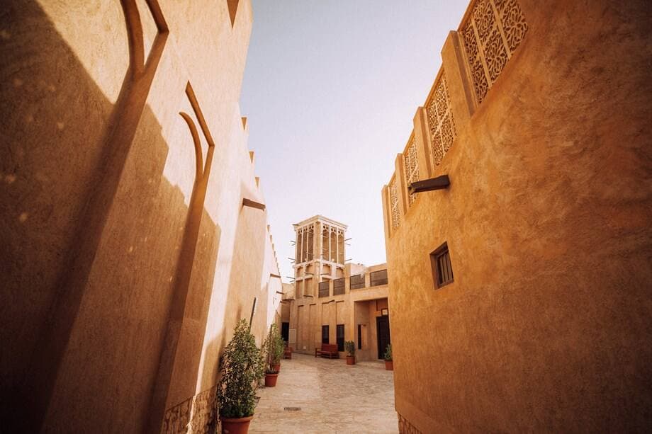 A narrow alley with traditional beige buildings and intricate wind towers under a clear blue sky, evoking a calm, historical atmosphere.