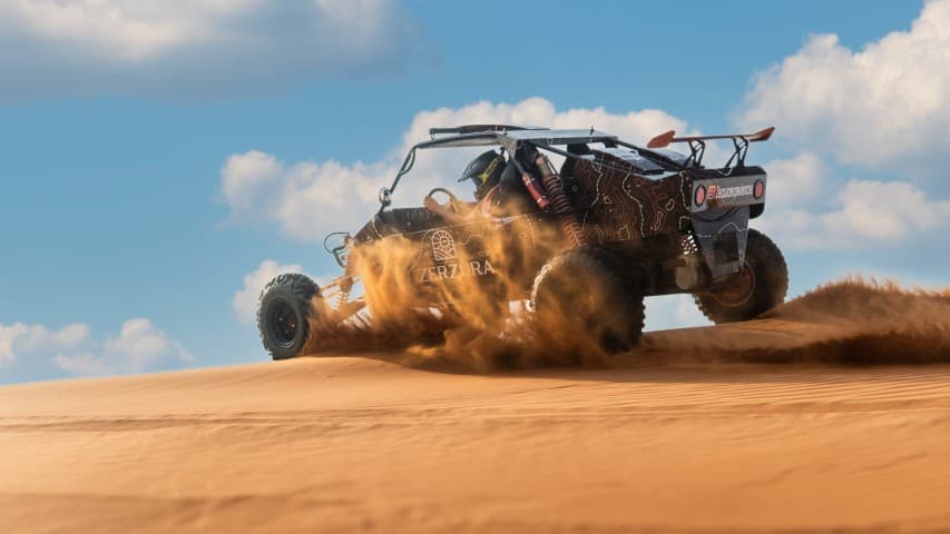 A man driving a desert buggy across sandy terrain during a buggy adventure with a camp dinner setup nearby.