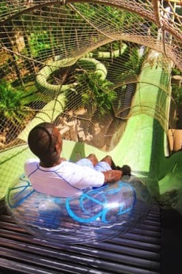 A man joyfully rides a water slide at Atlantis Aquaventure Water Park, splashing into the pool below.