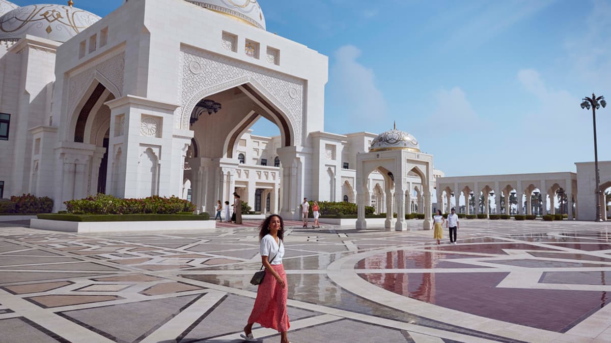 A woman walks in front of Qasr Al Watan in Abu Dhabi, showcasing a blend of architecture and urban life.