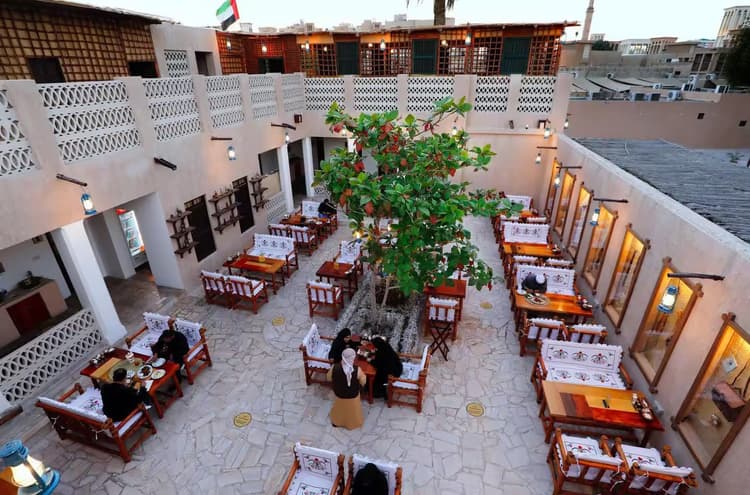 An open-air courtyard with patterned seating surrounds a central green tree. Guests dine at wooden tables.