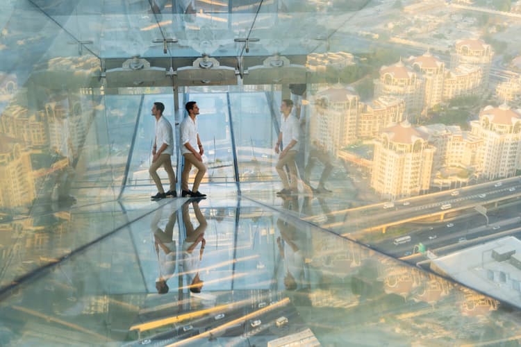 Visitor sliding through the glass slide at Sky Views Dubai with views of the city skyline