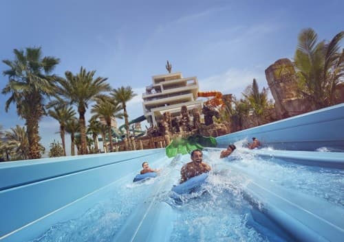 A group of people joyfully riding a water slide at Dolphin Kayak Dubai water park.
