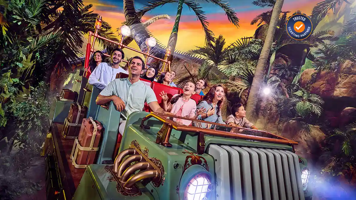 A group of people, including children and adults, smile excitedly while riding a jungle-themed amusement park ride at IMG Worlds of Adventure