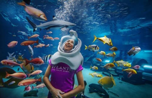 A woman in a helmet holds a fish while wading in water during Aqua Trek Xtreme Girl Aqua Trek event.