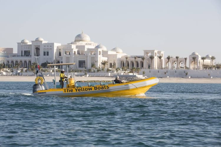A yellow and white boat floats in the water near Qasr Al Watan, a large building in Abu Dhabi.