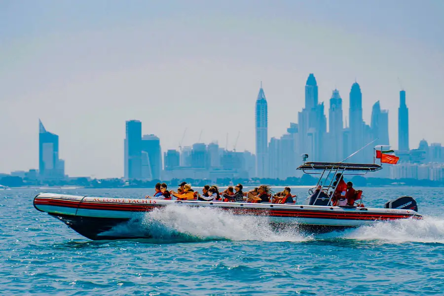 A speedboat with passengers in life jackets speeds across blue water, creating a wake.