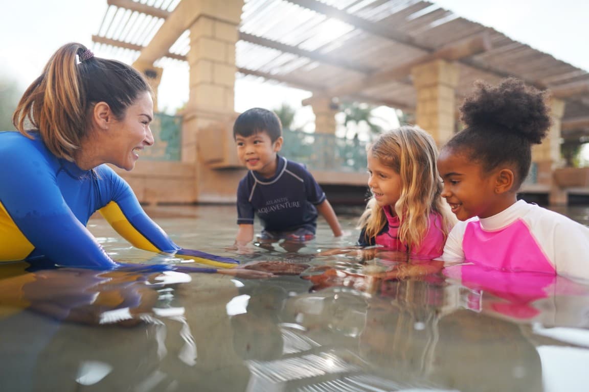 A woman and children enjoying a Dolphin Encounter at Atlantis Dubai, playing in the water at a resort.