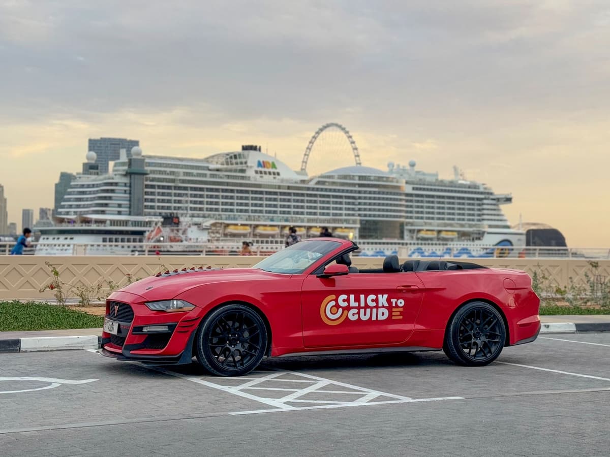 Red convertible sports car with "Click to Guide" logo parked by a waterfront.