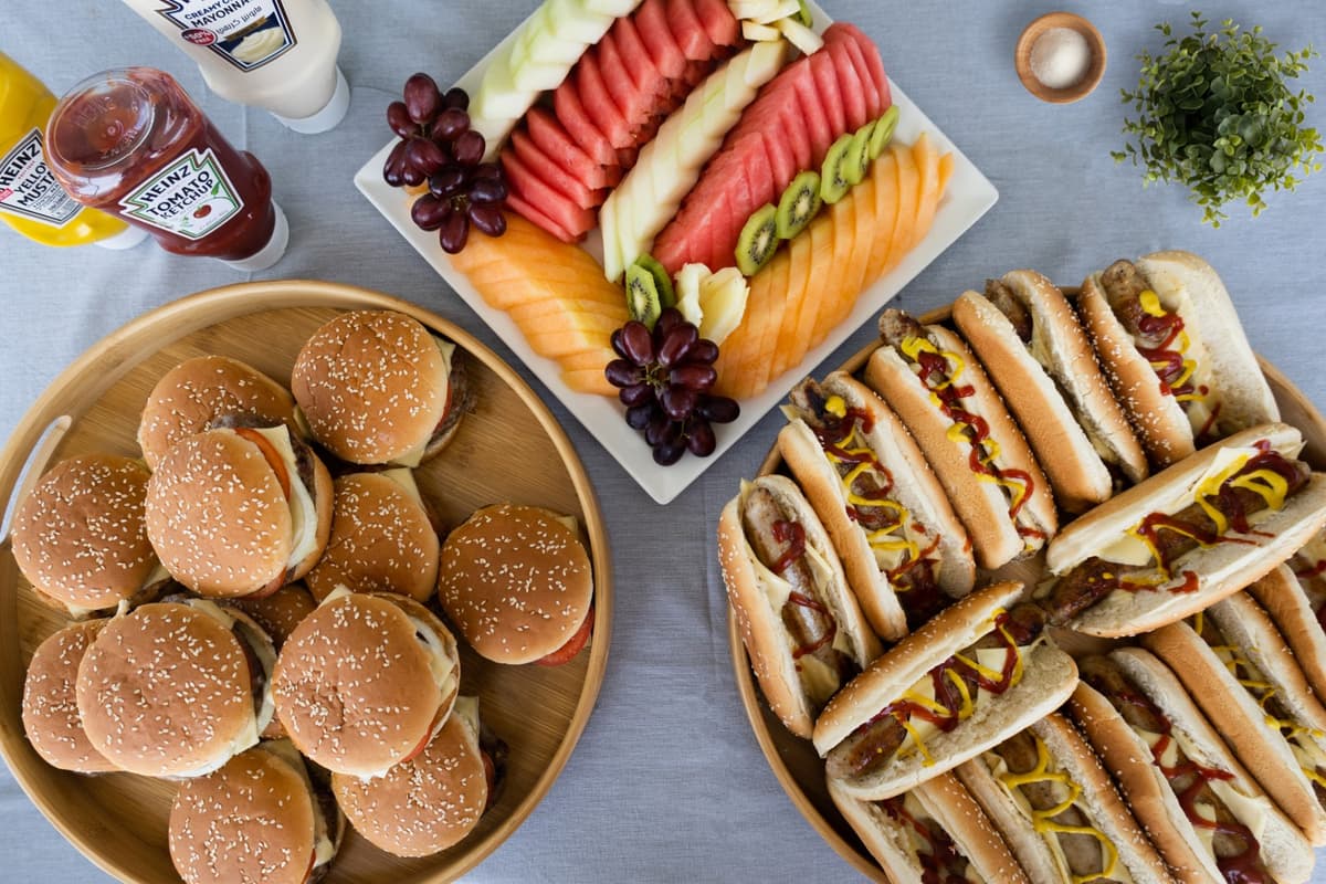 A table displaying an assortment of hot dogs alongside a variety of fresh fruits during the Burj Coastline Tour food event.