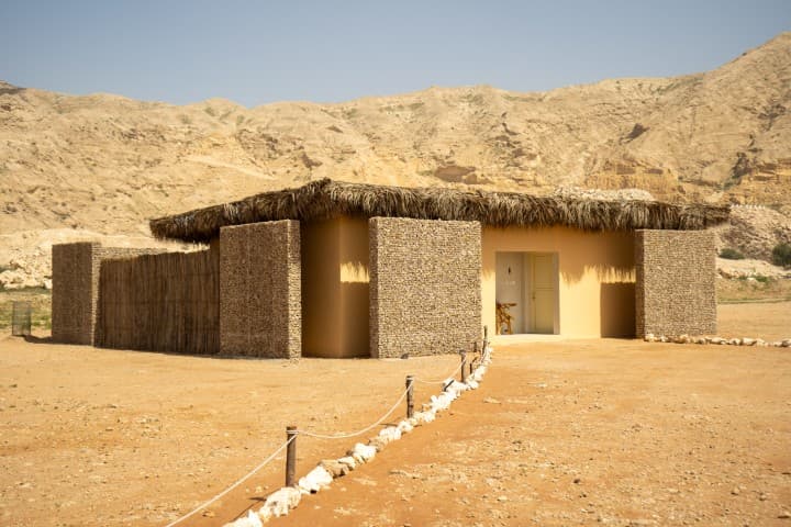 A small desert hut with a thatched roof surrounded by rocks, part of the Mleiha Buggy facility.